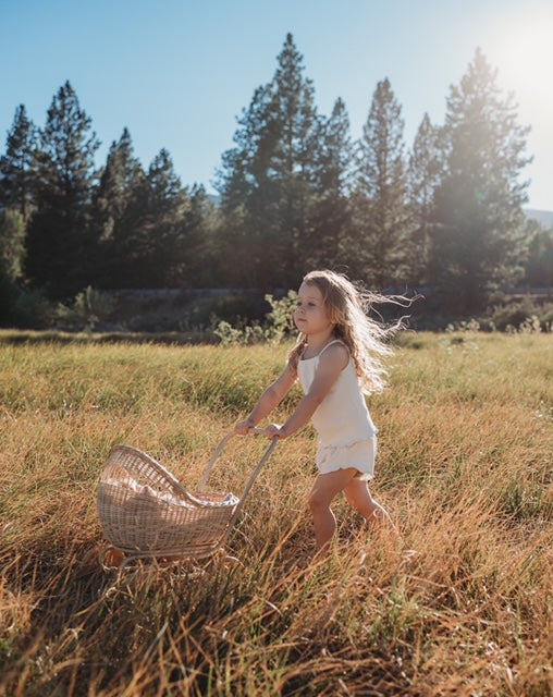 Child pushing a Poppie Rattan Doll Pram in a grassy field