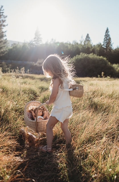 child playing with a doll and a Poppie Rattan Doll Pram in a sunny meadow