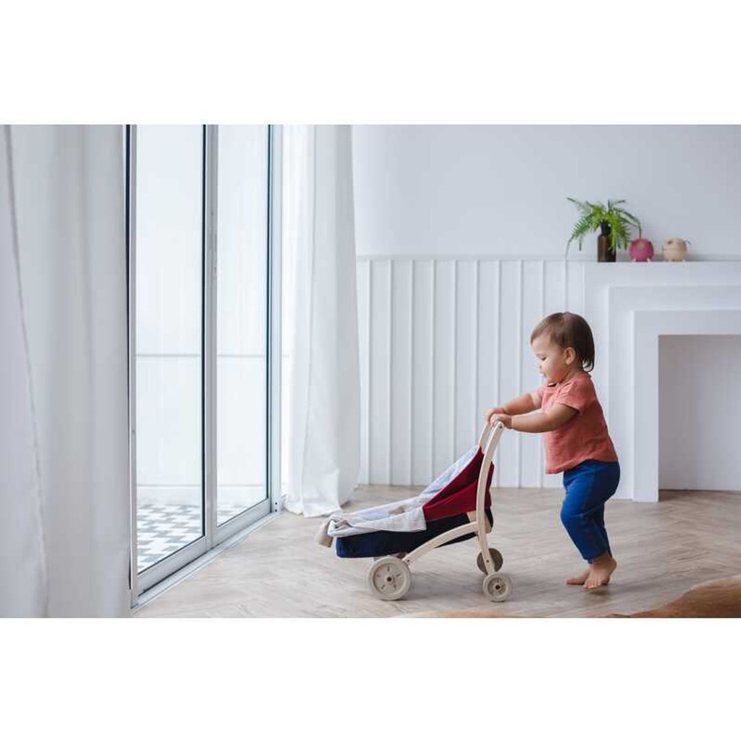 Toddler playing with a Doll Stroller by Plan Toys