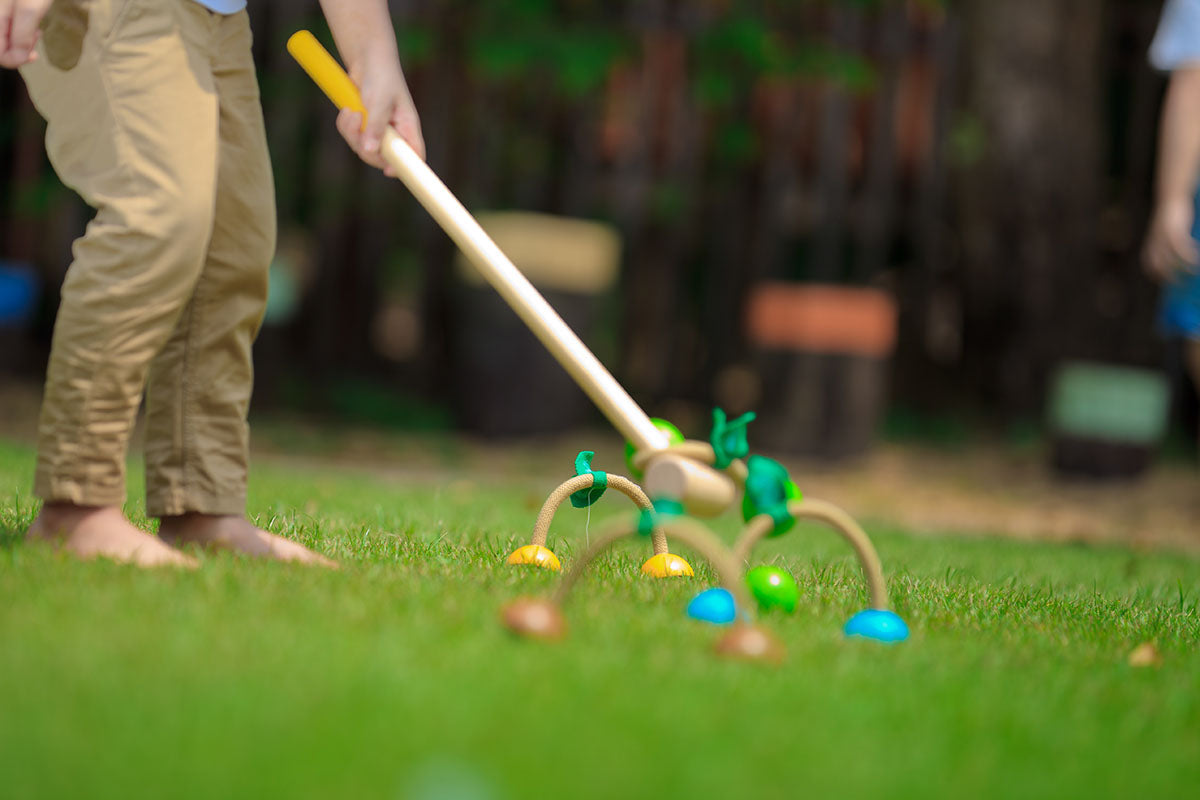 child playing on grass with a Croquet Set by Plan Toys