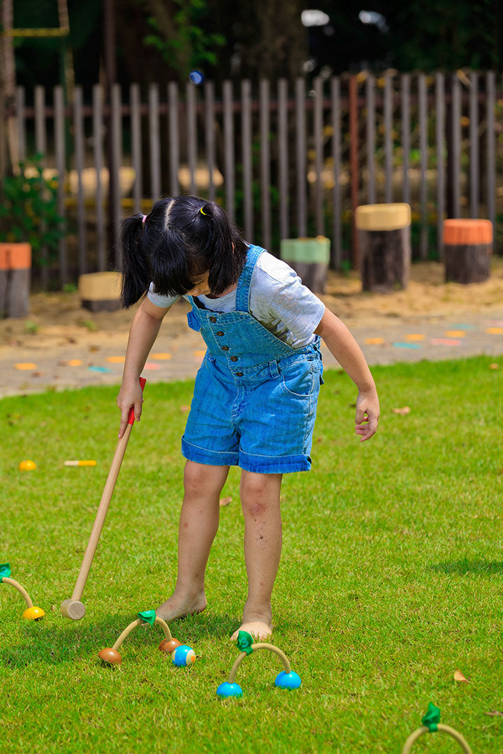 child playing outside with a Croquet Set by Plan Toys