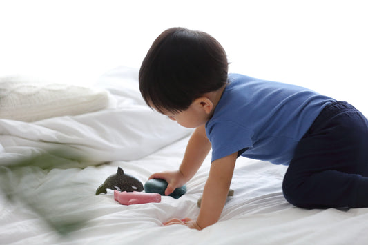 child crawling on a bed playing with small wooden sea creatures figures