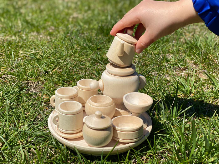 Child playing with wooden miniature tea set on grass