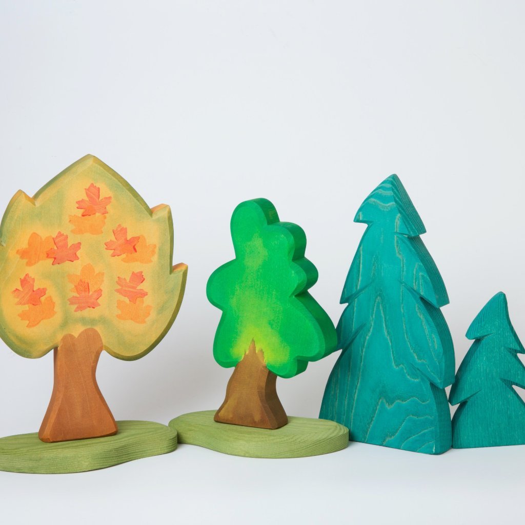 hand made and hand painted wooden trees standing side by side on a neutral back ground. The trees are a maple, and oak, a small and Large Spruce By Ostheimer