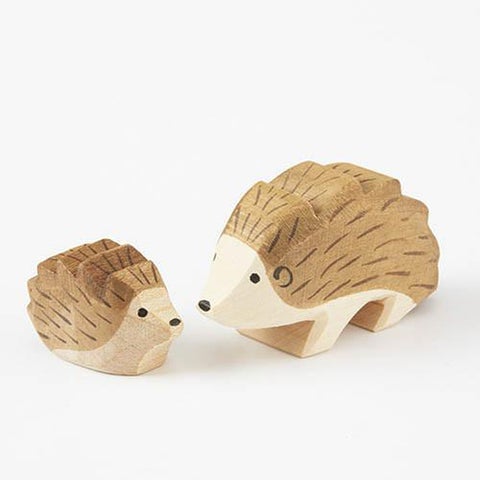 small and Large wooden hand carved Hedgehogs looking at each other on a white back ground