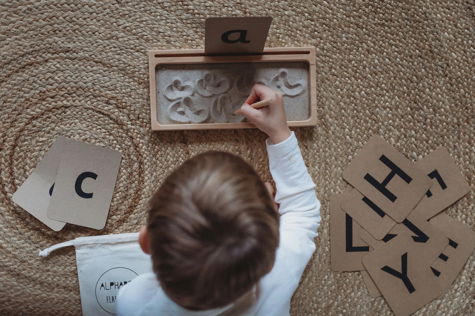 Kid practicing the letter "a" on a Sand Writing Tray