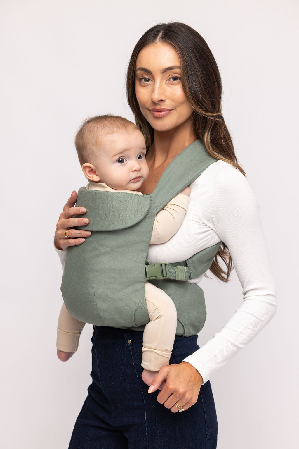 Woman holding a baby in a green baby carrier against a white background