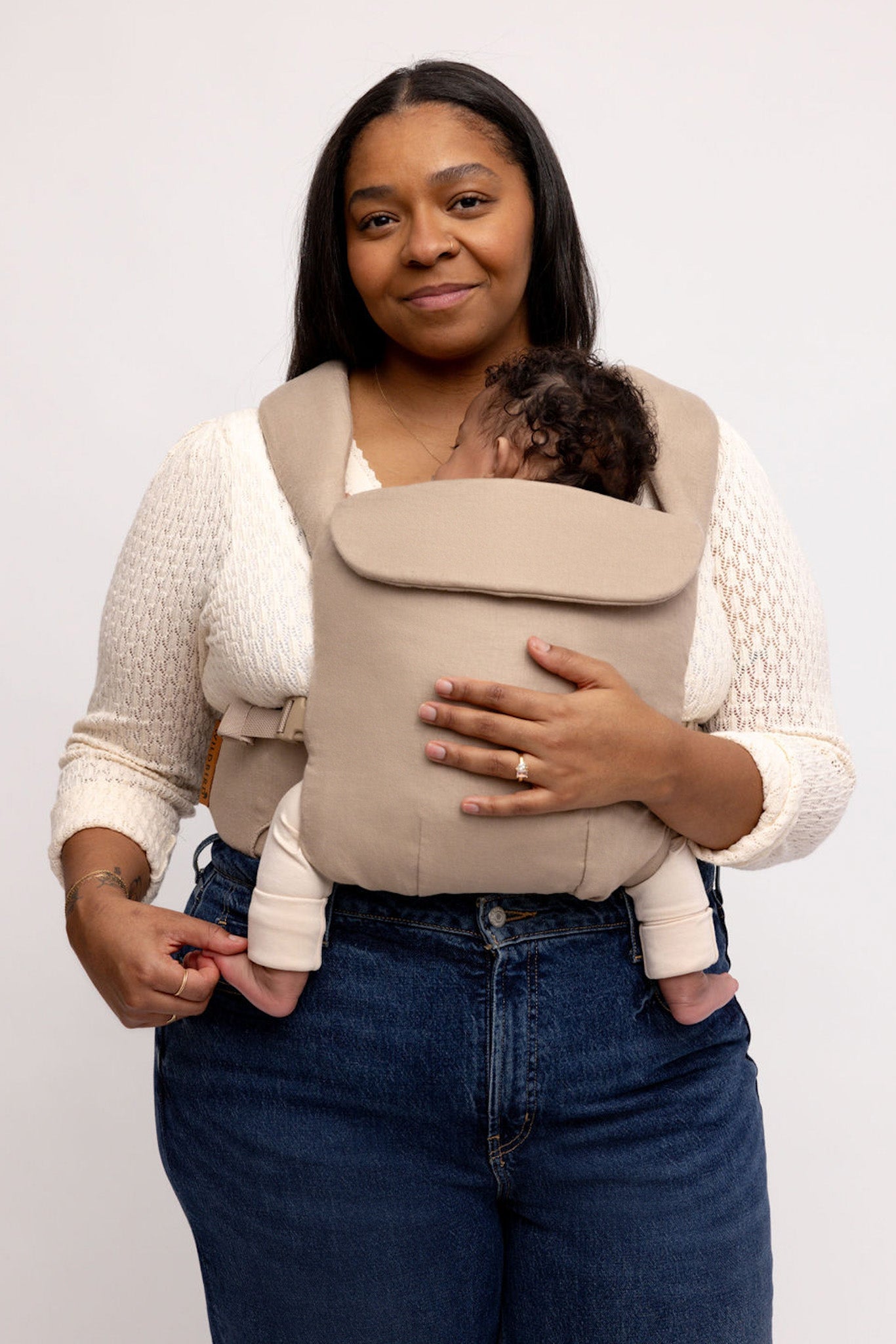 Woman holding a baby in a beige carrier against a white background