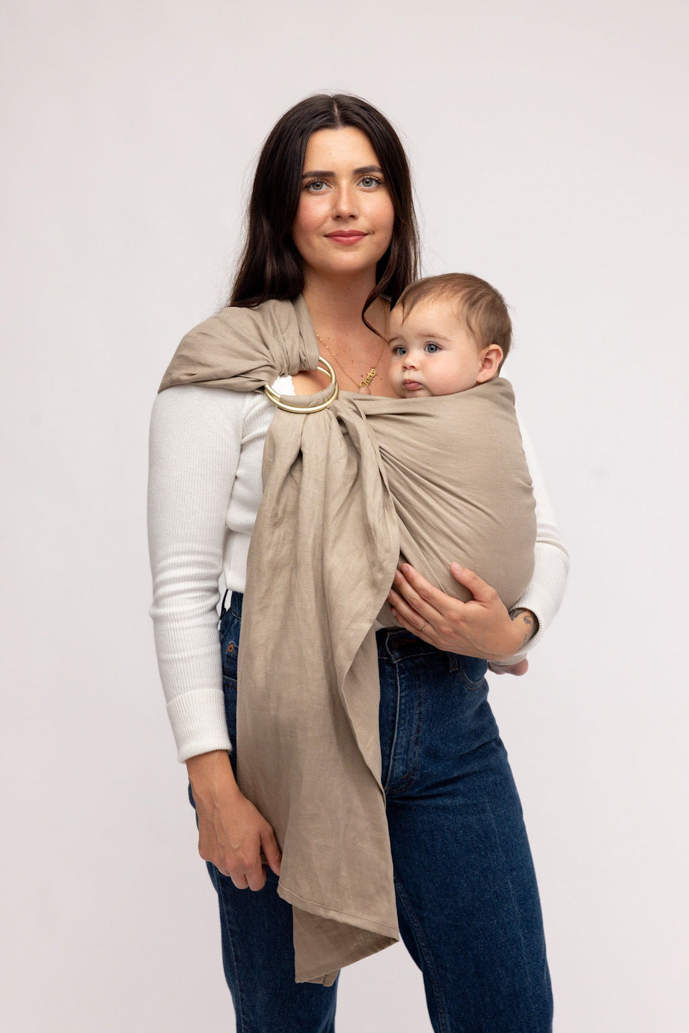 Woman holding a baby in a beige wrap against a white background