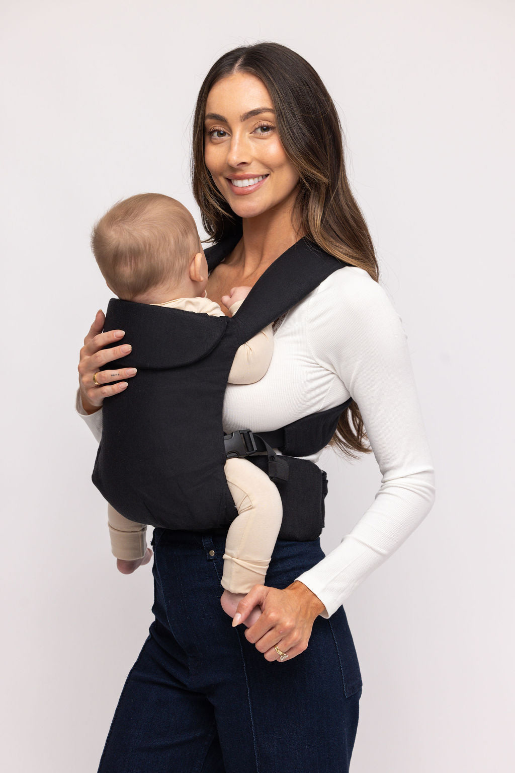 Woman holding a baby in a black baby carrier against a white background