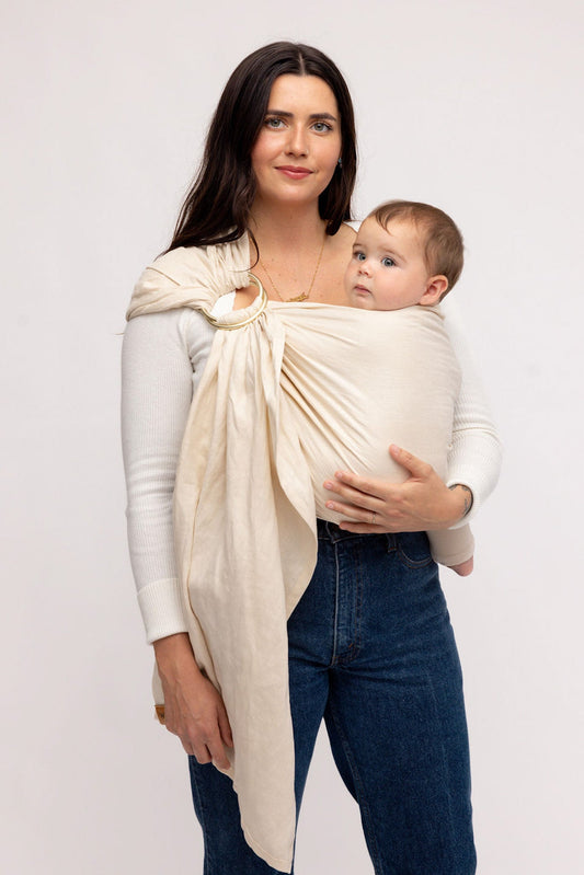 Woman holding a baby in a beige baby wrap against a white background
