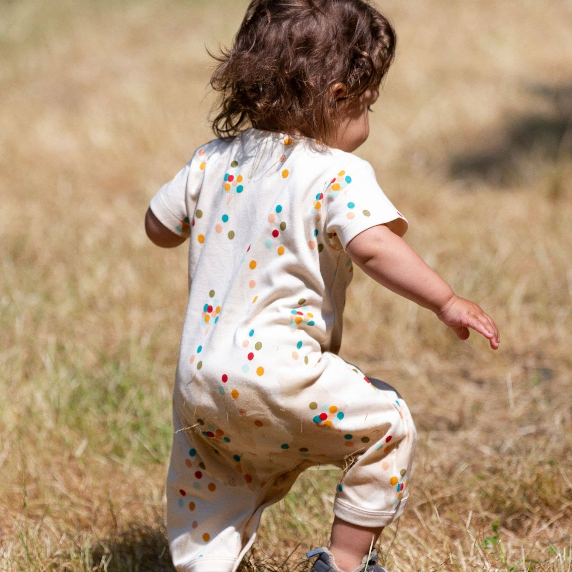 Baby running in a grass field wearing Rainbow Balloons Organic Summer Romper