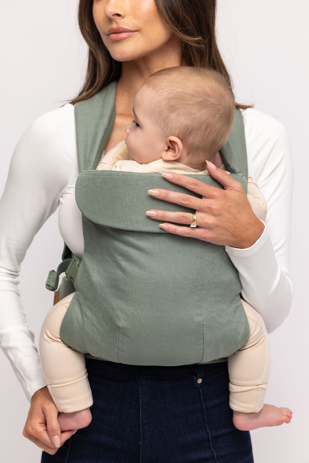 Woman holding a baby in a green baby carrier against a white background