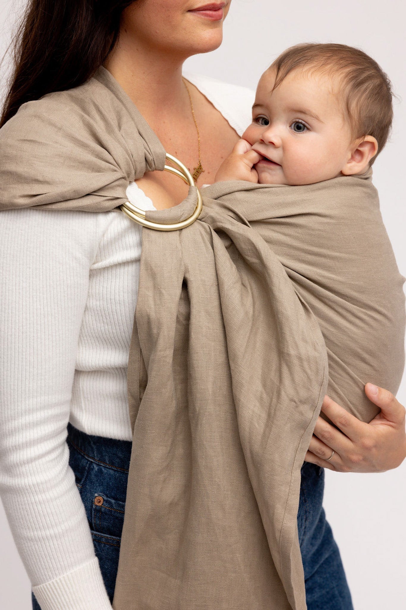 Woman holding a baby wrapped in a beige wrap against a white background
