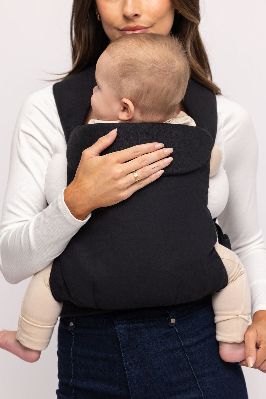 Woman holding a baby in a black carrier against a white background