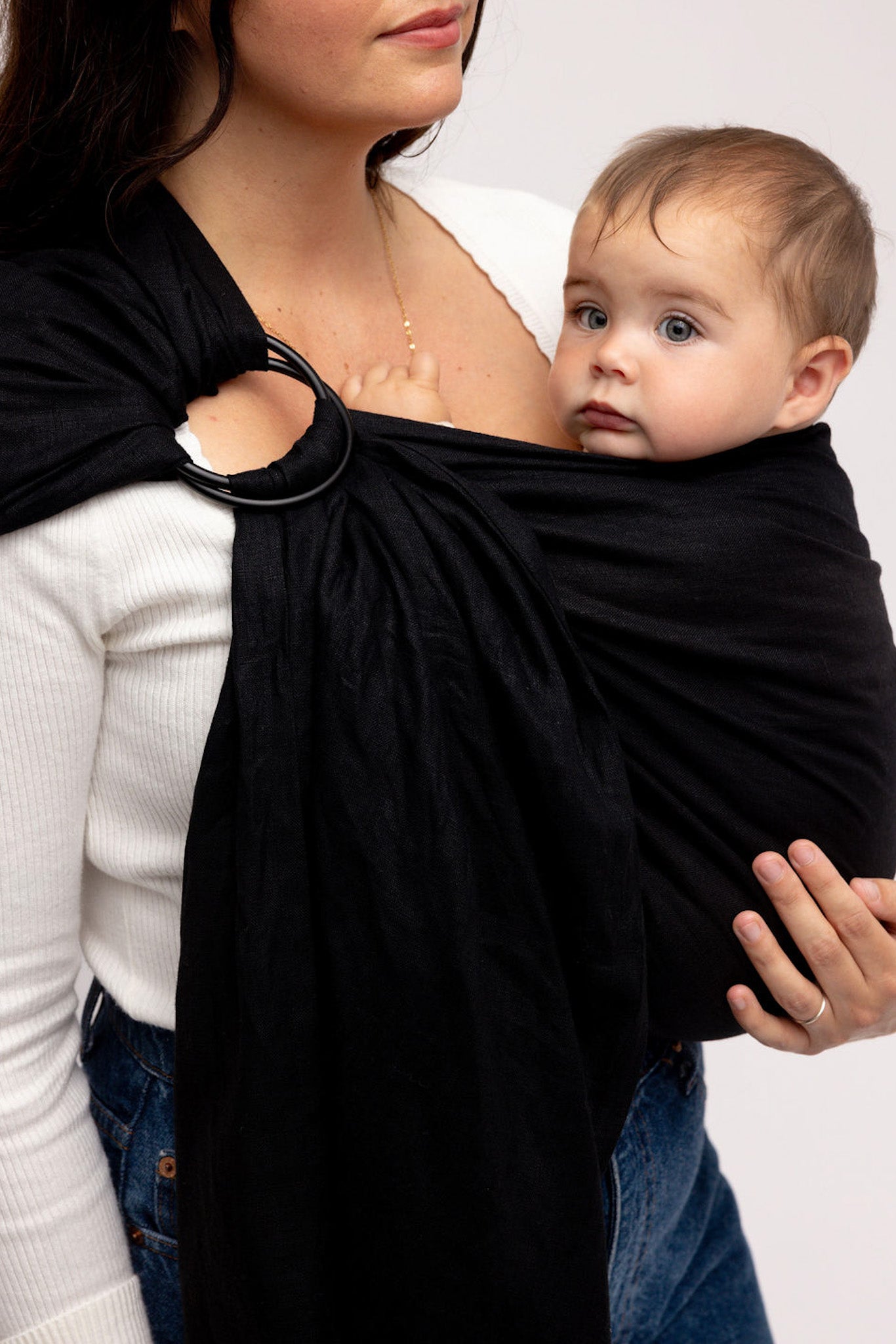 Woman holding a baby in a black sling against a plain background