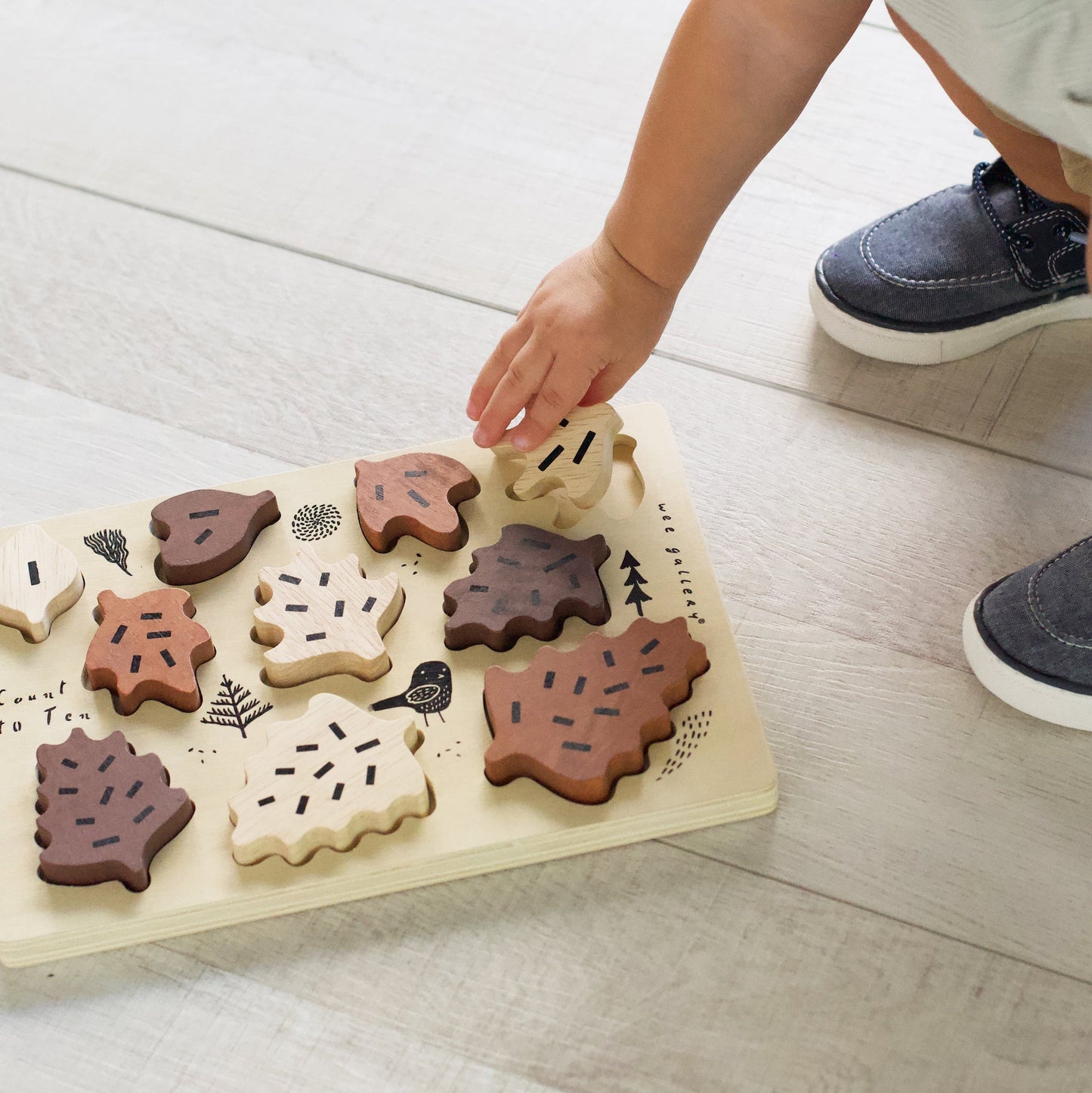 Child playing with a wooden leaf puzzle on a light wooden floor.