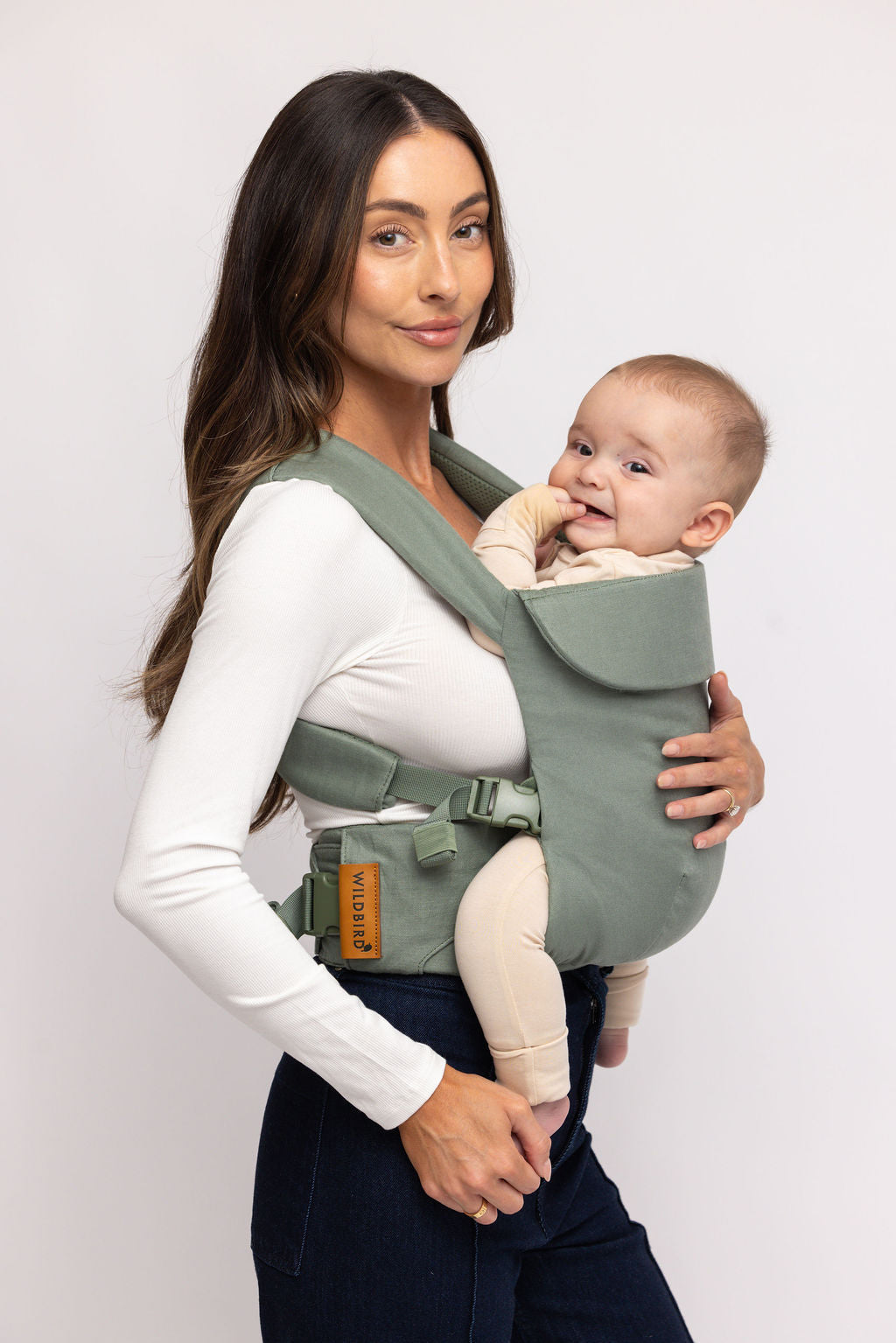 Woman holding a baby in a green baby carrier against a white background
