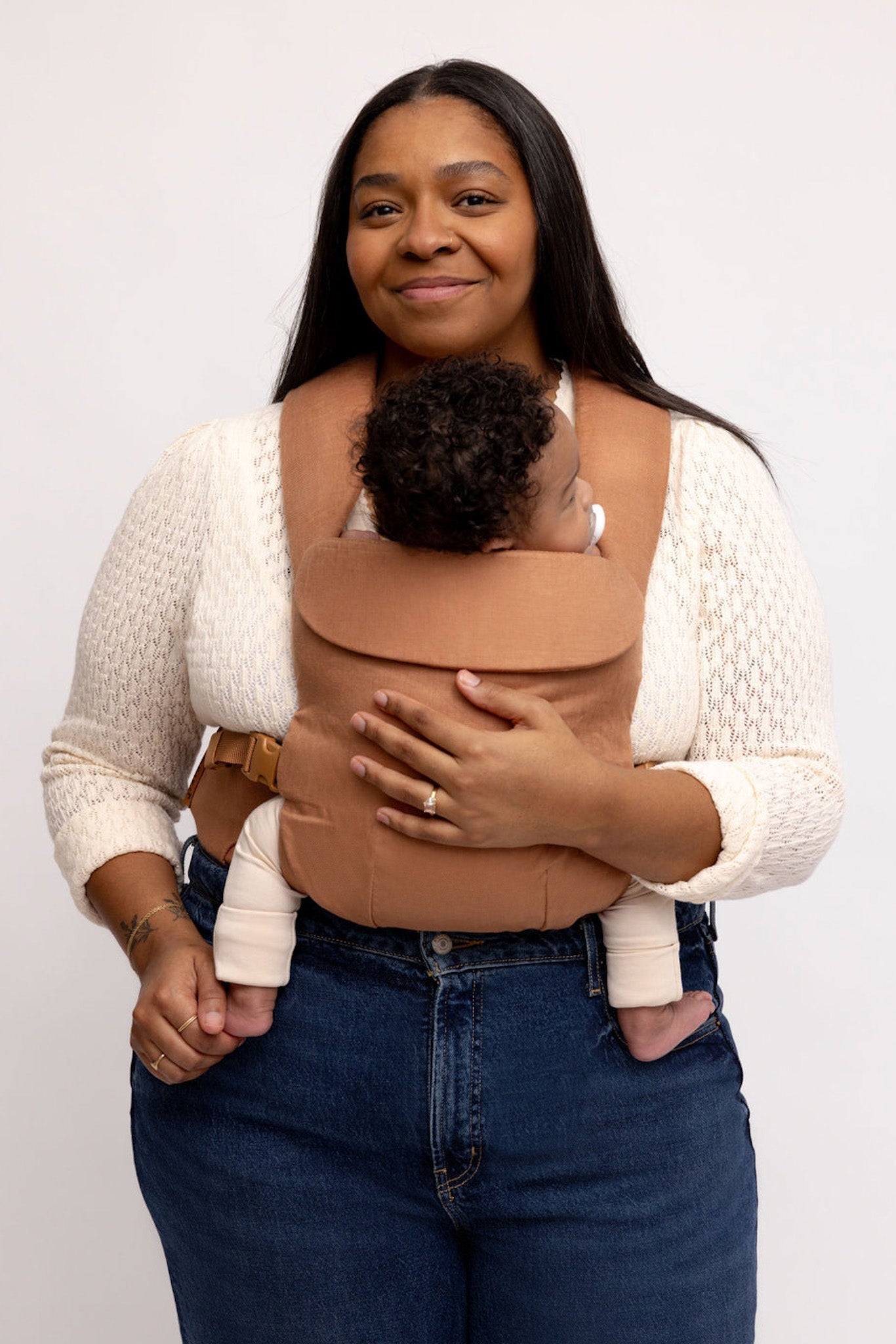 Woman holding a baby in a brown baby carrier against a white background