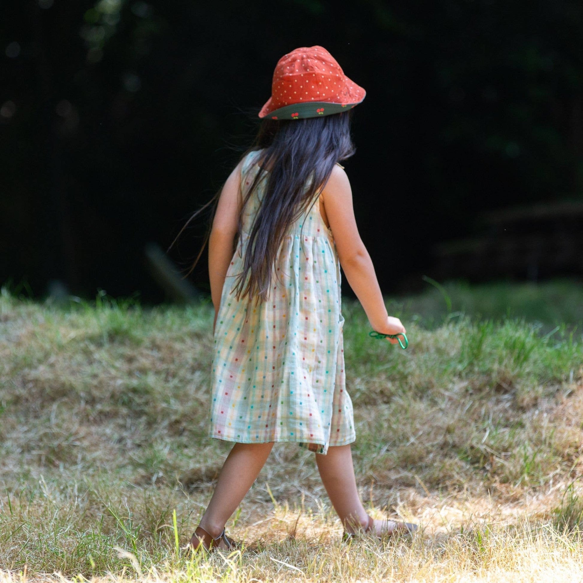 Child walking in a grass field wearing Cherries Reversible Sunhat in Olive