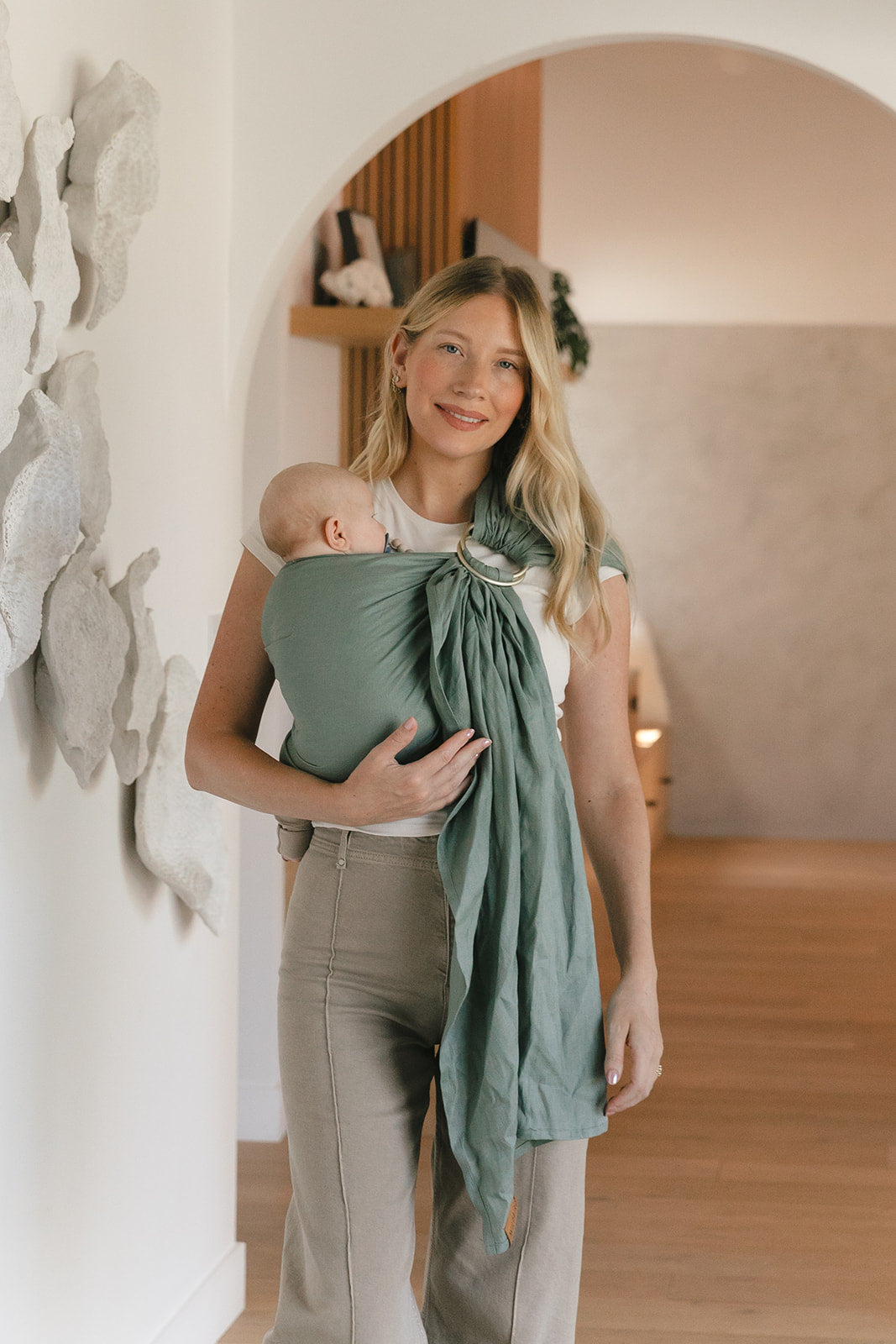 Woman holding a baby wrapped in a green sling in a home setting