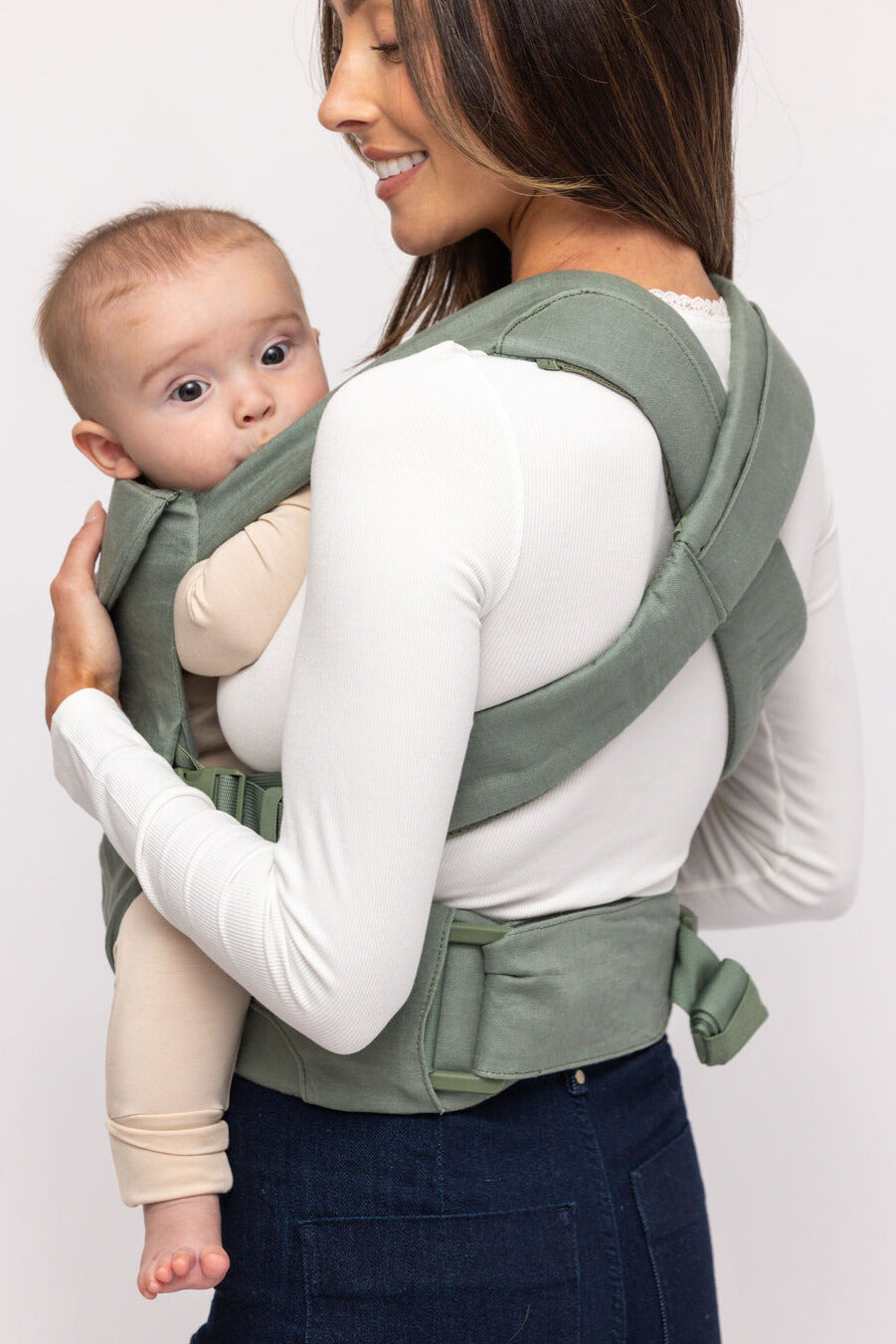 Woman carrying a baby in a green baby carrier against a white background