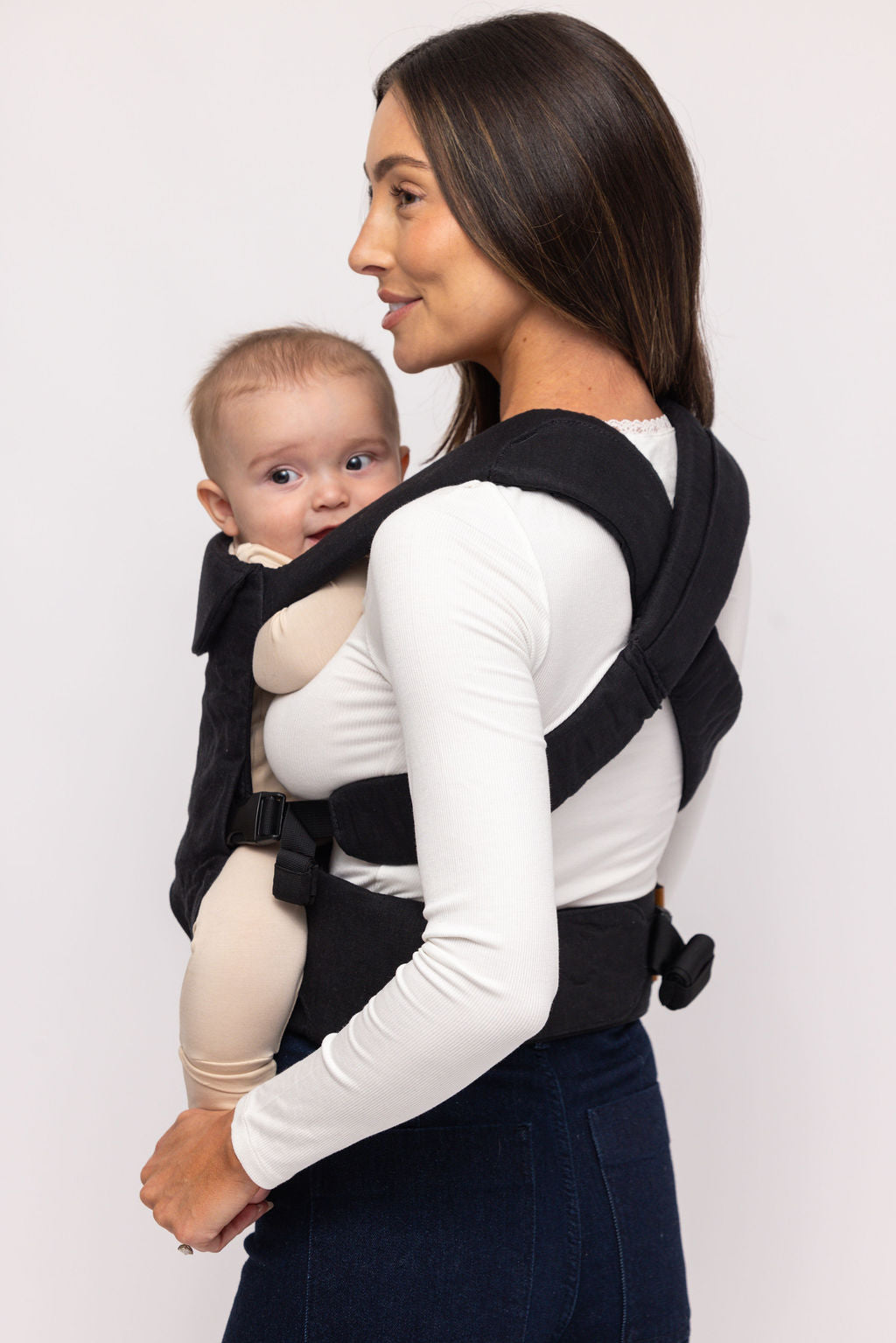Woman carrying a baby in a black baby carrier against a white background