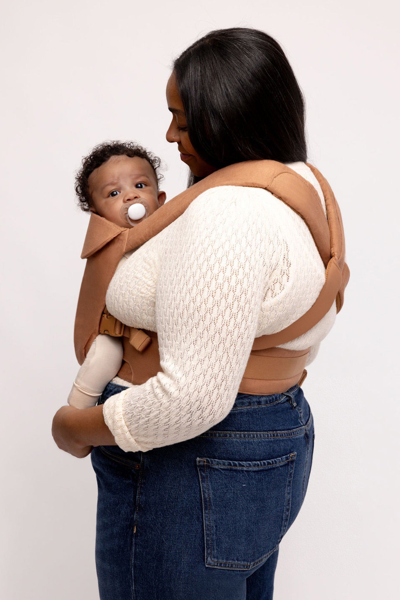 Woman carrying a baby in a brown baby carrier against a white background