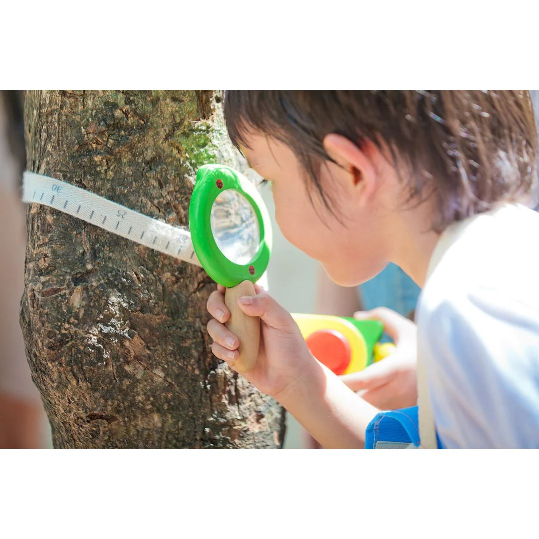child looking at a measuring tape wrapped around a tree through a leaf magnifier