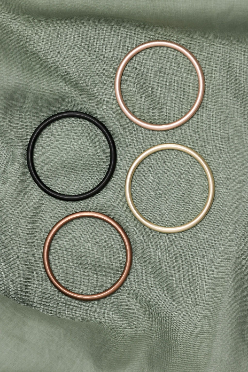 Four metal rings in black, rose gold, and gold on a green fabric background