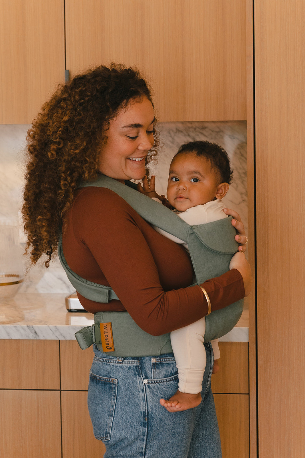 Woman holding a baby in a carrier in a kitchen setting