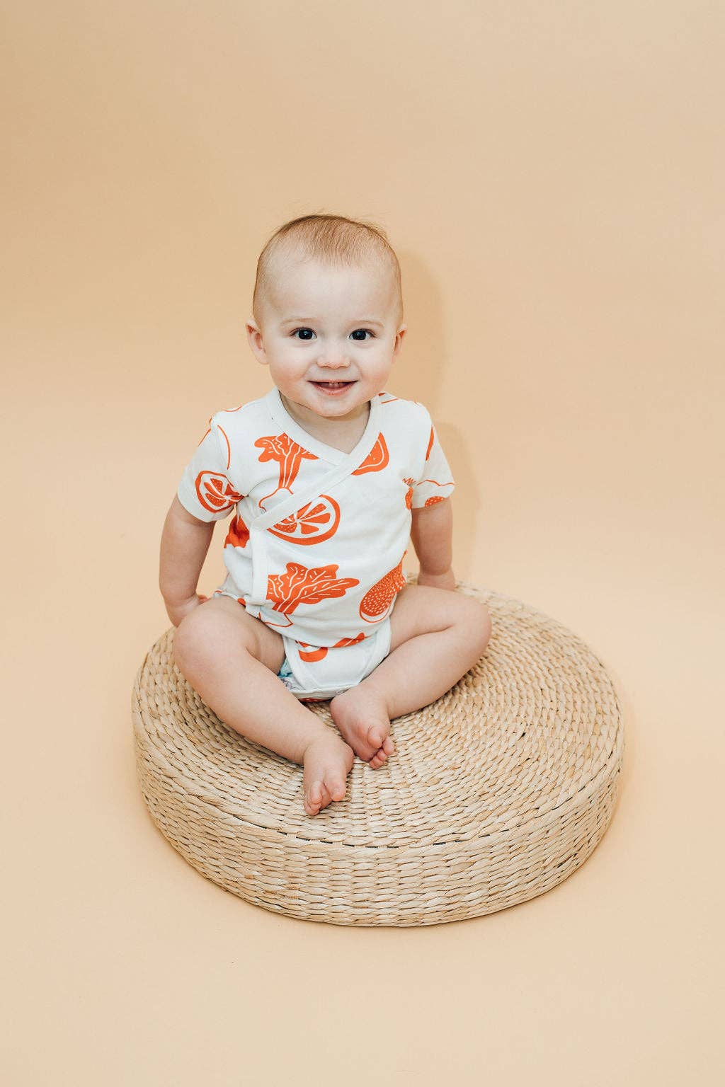 Baby sitting on a straw basket wearing fruit baby bodysuit