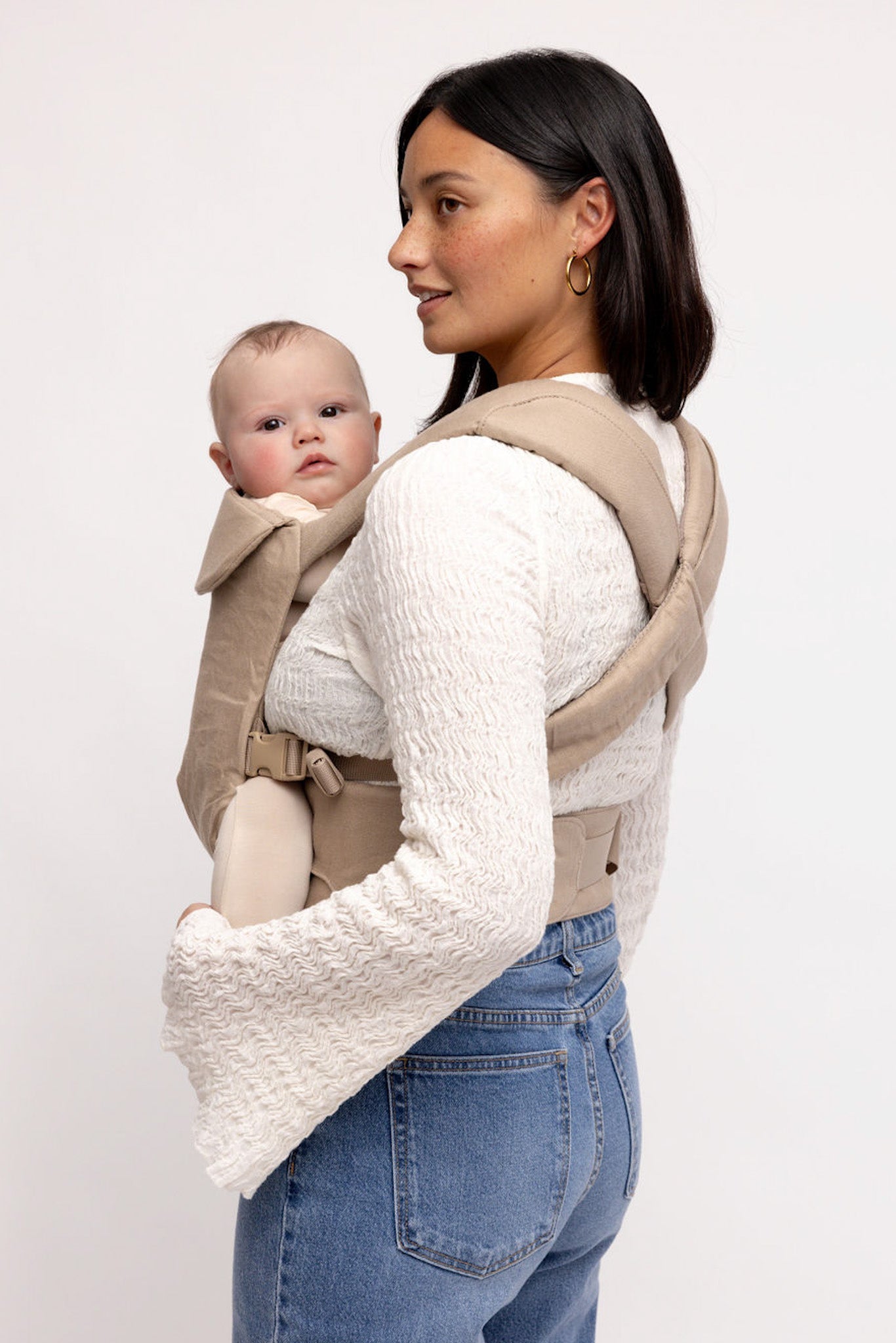 Woman carrying a baby in a beige baby carrier against a white background