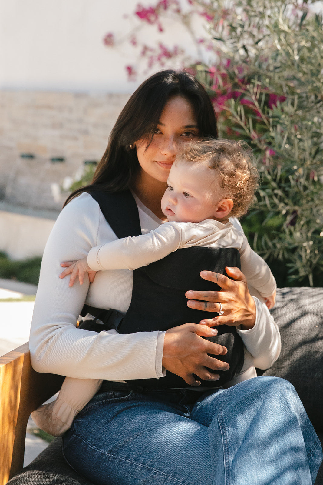 Woman holding a child in a carrier outdoors with plants in the background