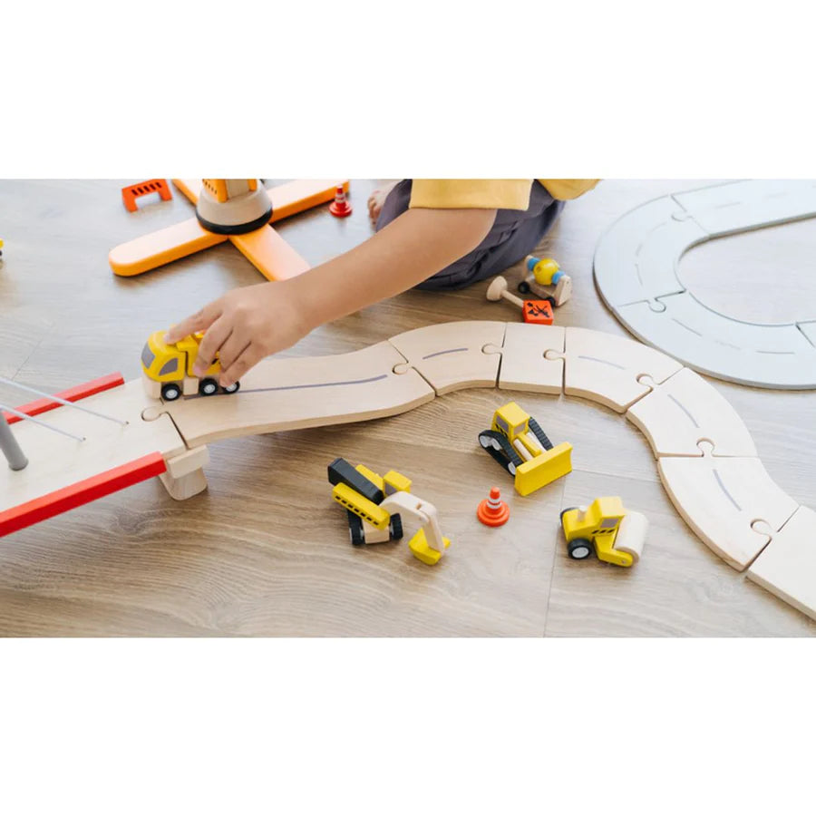 child playing with road construction vehicles and wooden road set