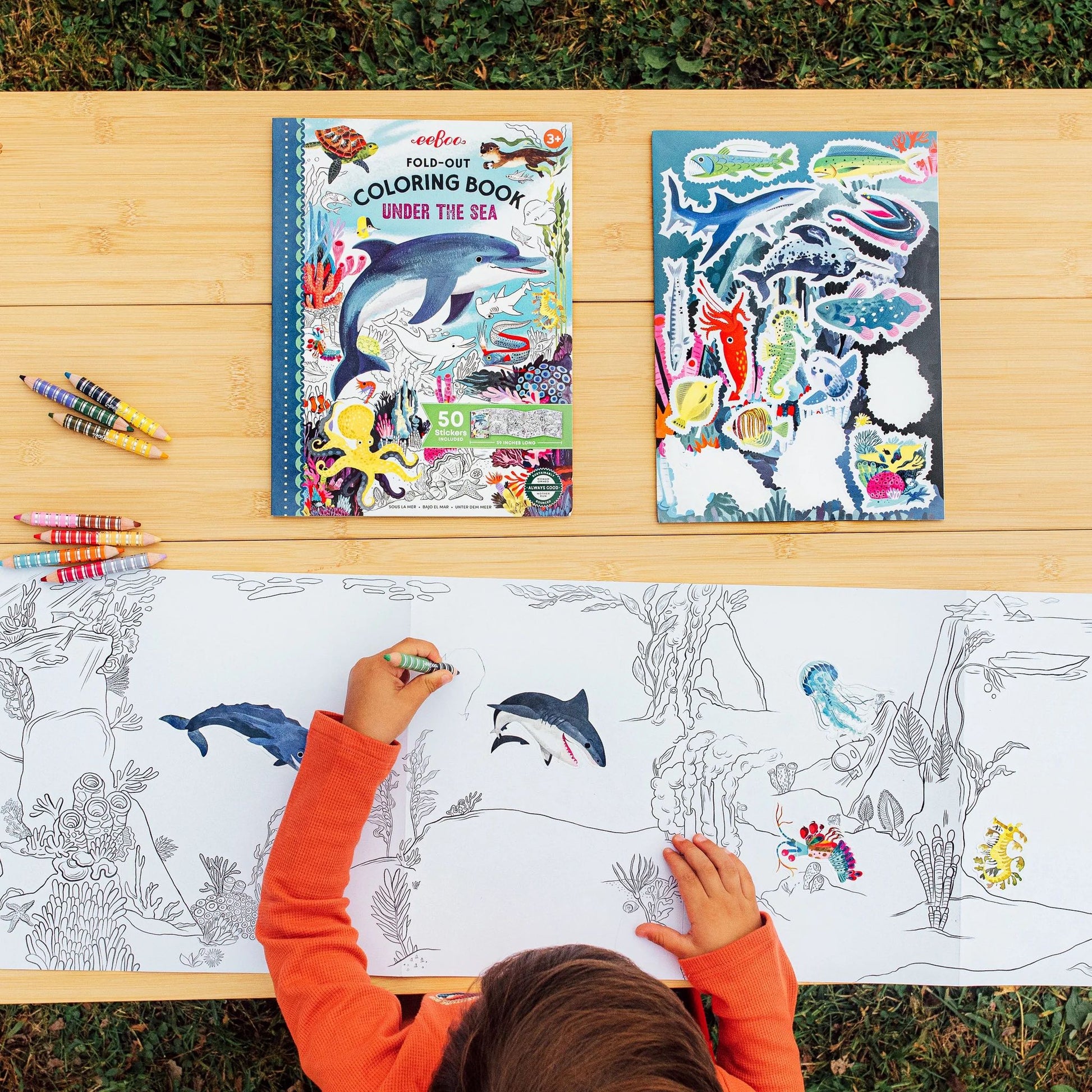 a child sitting outdoors coloring in a Under the Sea fold-out coloring book opened on a wooden table 
