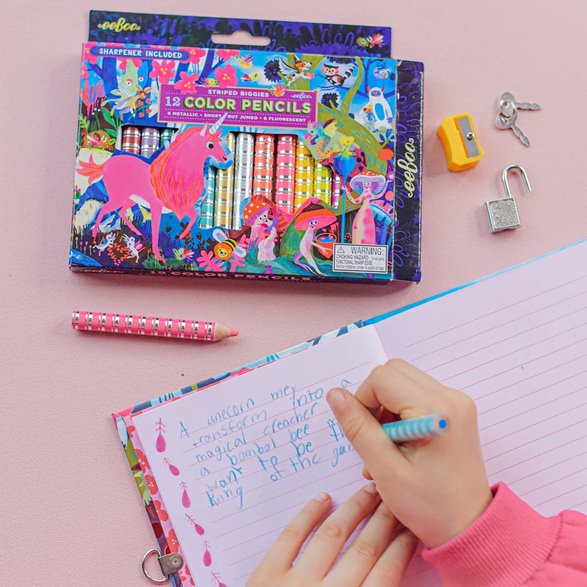 Child wearing a pink sweater writing in a journal with a blue metallic pencil