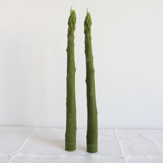 Two green asparagus-like candles on a white surface