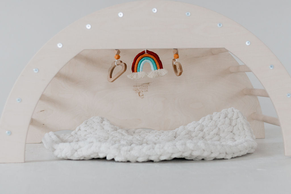 Wooden arch with knitted white blanket and decorative items on a light gray background