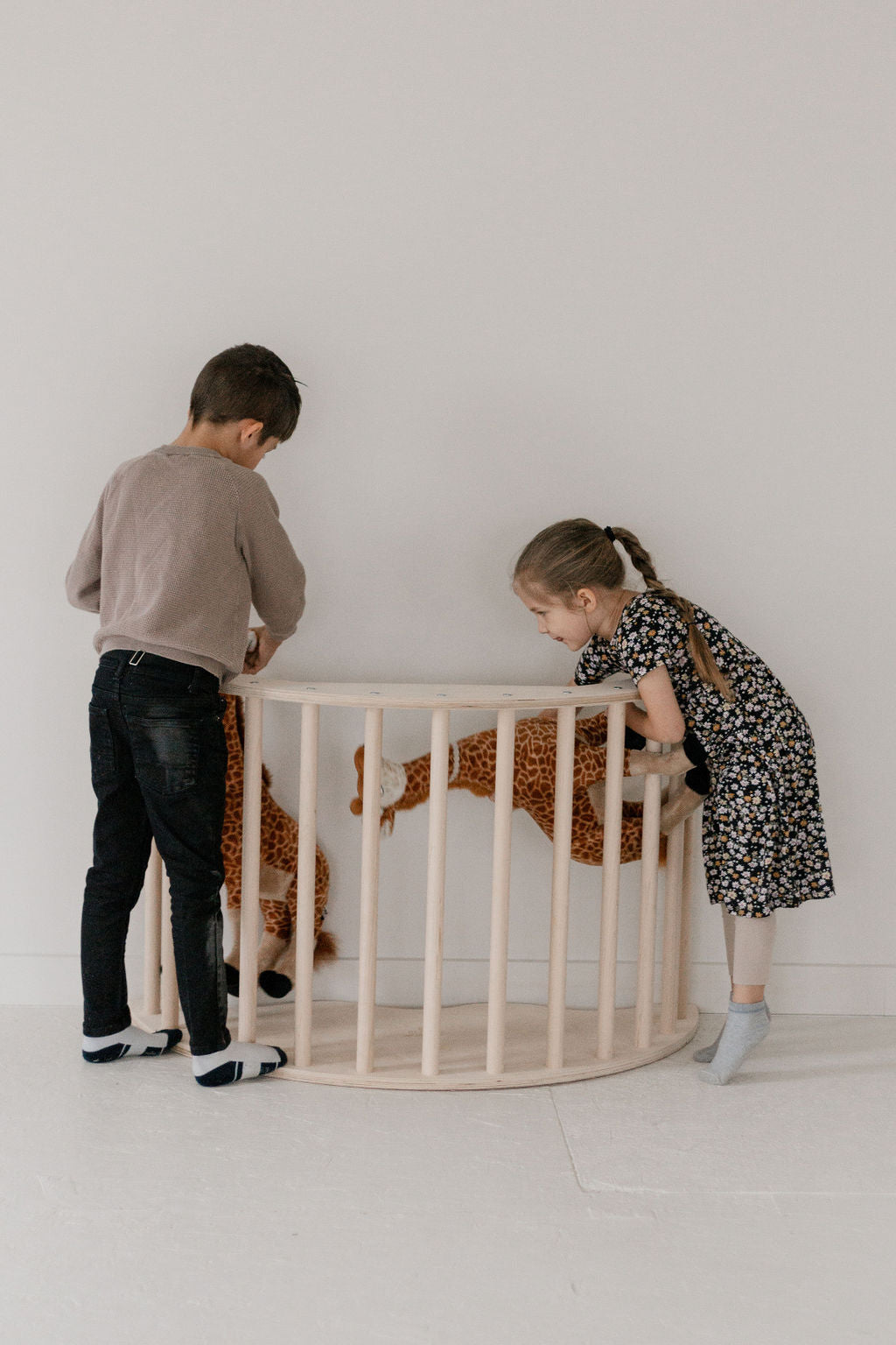 Two children interacting with a wooden crib in a minimalistic room.