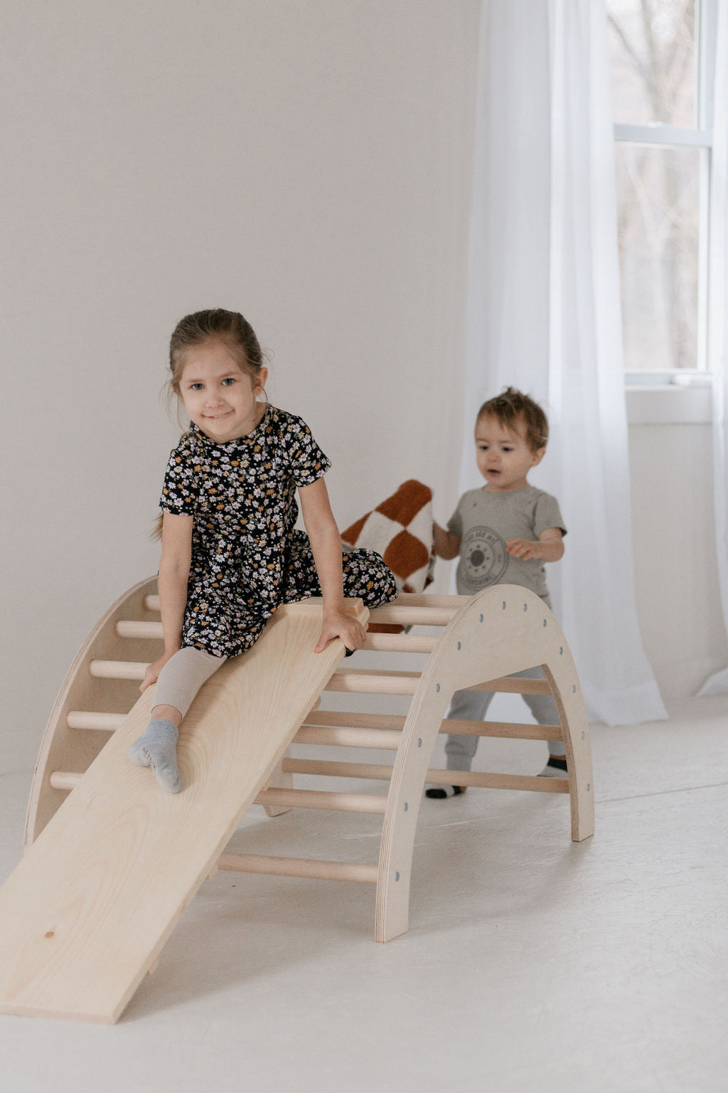 Two children playing on a wooden climbing toy in a bright room.