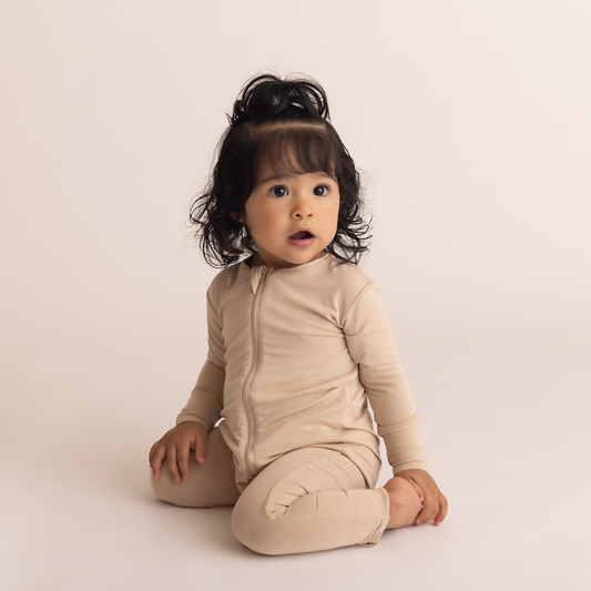 Baby wearing a beige romper sitting on a plain background