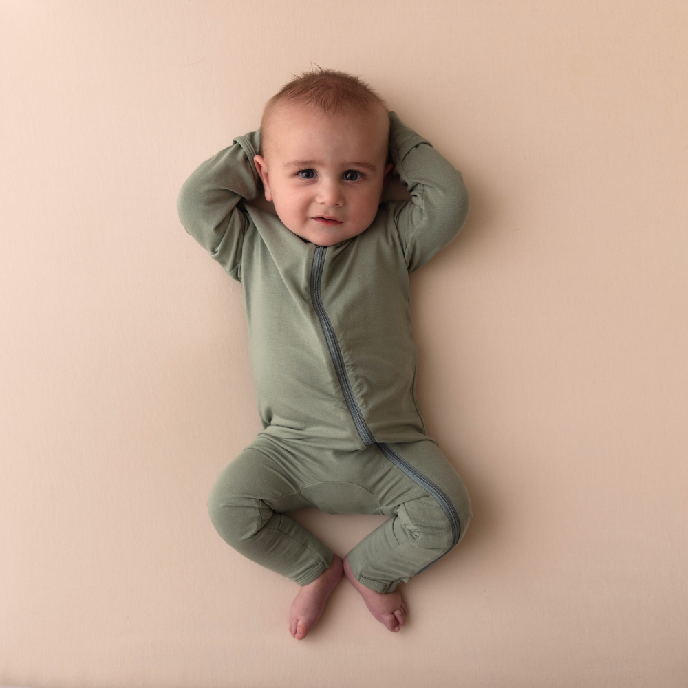 Baby wearing a green romper on a beige background