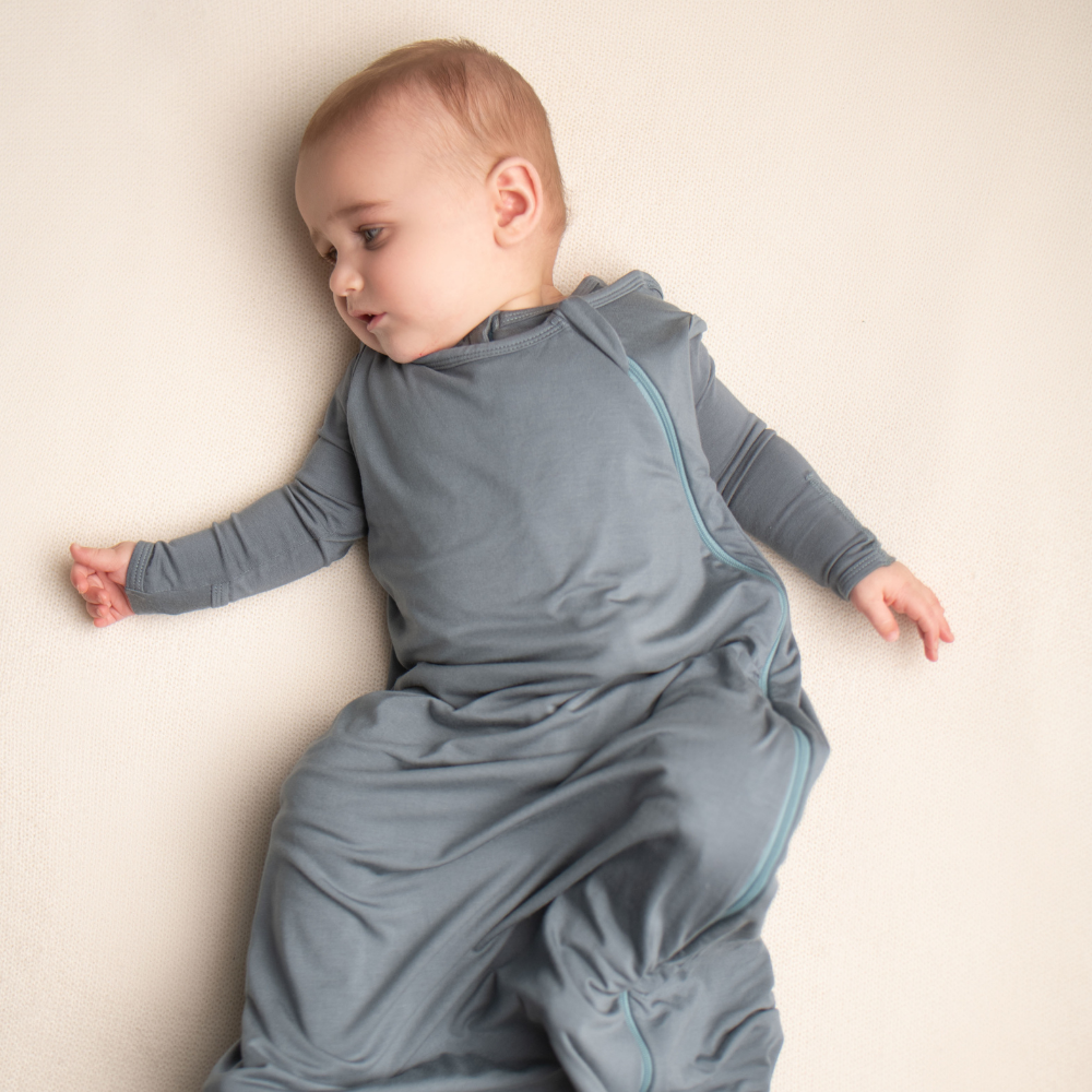Baby wearing a gray onesie with a zipper on a beige background