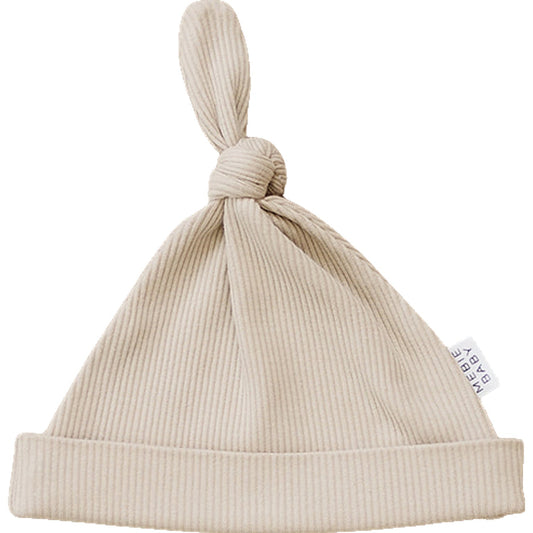 Beige baby hat with knot on top and a visible brand tag on a white background
