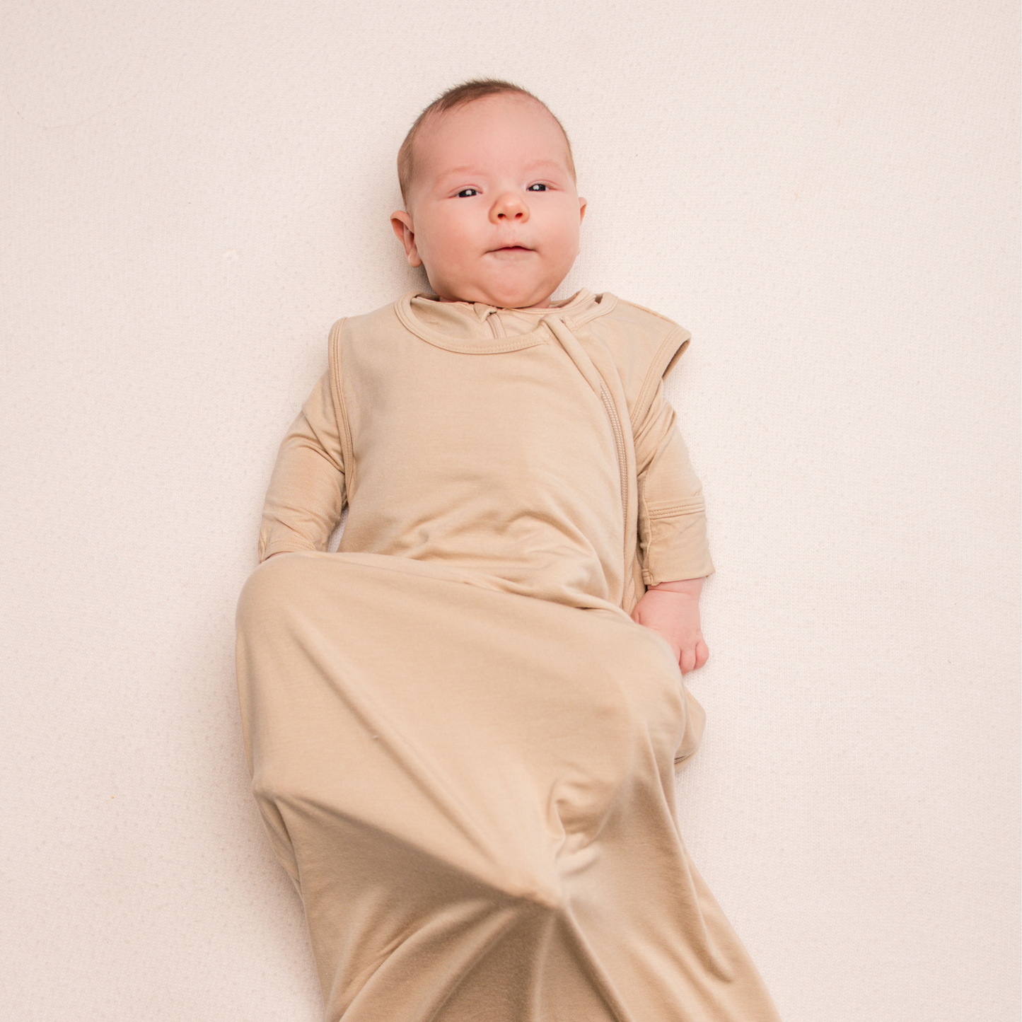 Baby wrapped in a beige swaddle on a plain background