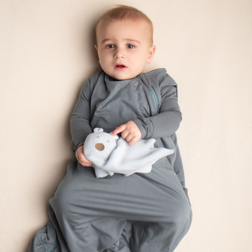 Baby in a gray outfit holding a white plush toy against a beige background