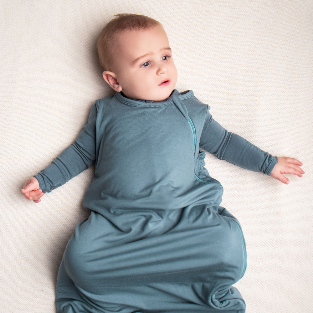 Baby in a blue sleep bag lying on a white surface