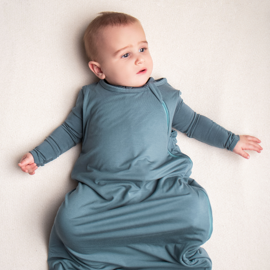 Baby in a blue sleep bag lying on a white surface