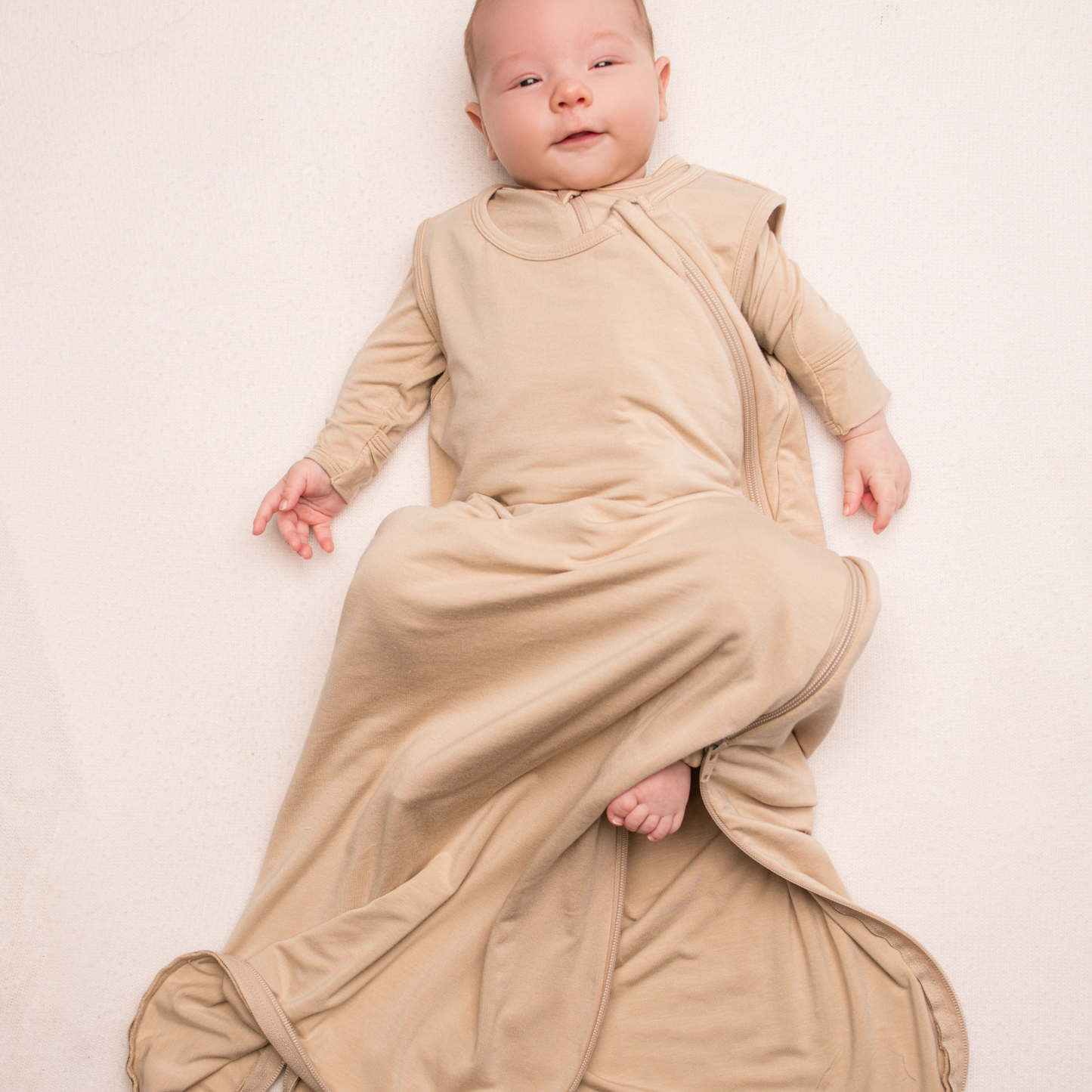 Baby wrapped in a beige swaddle on a plain background